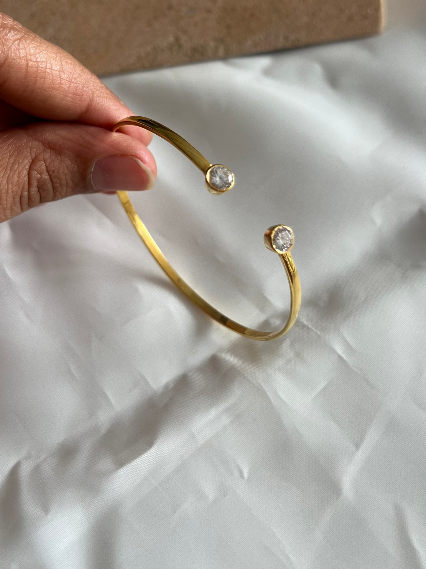 Gold bracelet with small stones held by a hand on a white surface
